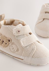 Beige baby schoen van ribfluweel met dubbele klittenbandsluitingen en geborduurde teddybeergezichten aan de zijkant en op de neus.