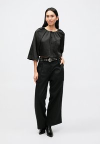 Schwarze, kurz geschnittene Bluse mit weiten Ärmeln und durchgehender Knopfleiste. Kombiniert mit hoch taillierten, schwarzen, weit geschnittenen Hosen und einem mit Nieten besetzten Gürtel.