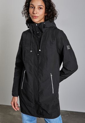 Veste légère noire avec capuche, poches latérales zippées et cordons de serrage. Présente une finition texturée et un logo "STREET ONE" sur la manche.