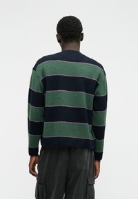 Maglione a righe nei colori verde scuro e blu navy, con sottili linee orizzontali rosa. Texture a maglia e scollo a girocollo.