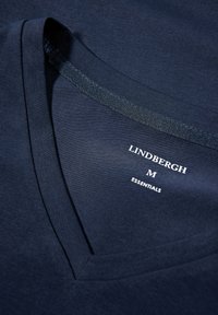 Marineblaues kurzärmliges T-Shirt mit V-Ausschnitt, aus glattem Stoff. Enthält weißen Markentext: "LINDBERGH M ESSENTIALS."