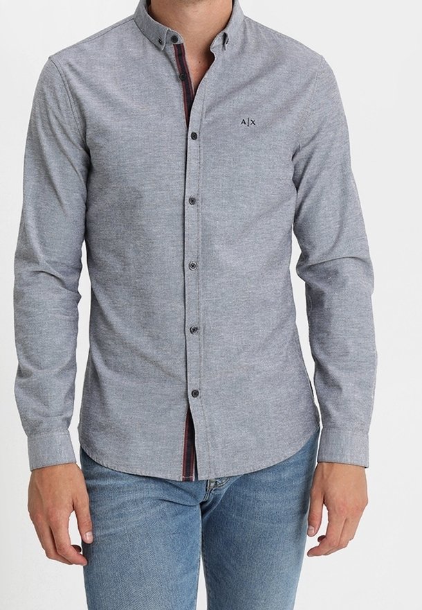 Jasnoszara koszula na guziki z długim rękawem i ostrym kołnierzykiem, z delikatną fakturą i małym czarnym logo na piersi.