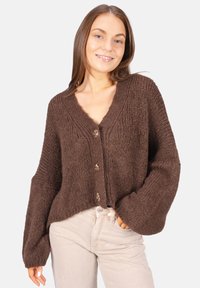 Brauner, gestrickter Cardigan mit V-Ausschnitt, langen Ärmeln und fünf Knöpfen. Strukturiertes Material und lässige Passform, kombiniert mit hellen Jeans.