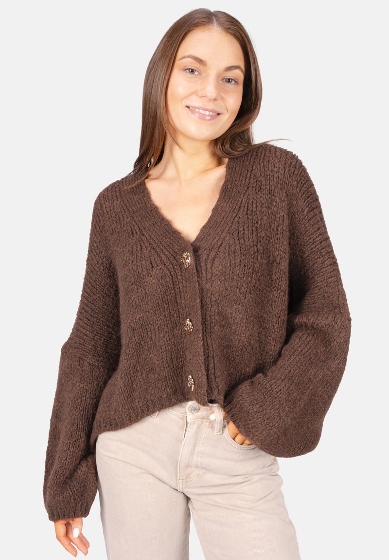 Brauner, gestrickter Cardigan mit V-Ausschnitt, langen Ärmeln und fünf Knöpfen. Strukturiertes Material und lässige Passform, kombiniert mit hellen Jeans.