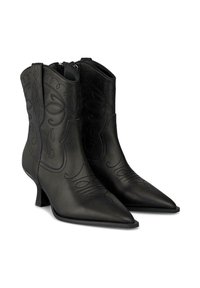 Botas de piel negra hasta el tobillo con punteras afiladas, intrincados diseños grabados y un tacón bajo para mayor estabilidad. Cierre con cremallera en la parte posterior.