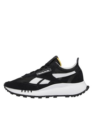 Czarno-białe buty sportowe Reebok z grubą białą podeszwą, siateczkową i zamszową cholewką, białymi paskami z logo oraz małym żółtym detalem na języku.