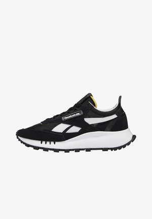 Sneaker Reebok bianco e nero con suola bianca spessa, tomaia in mesh e suede, strisce bianche con logo e piccolo dettaglio giallo sulla linguetta.