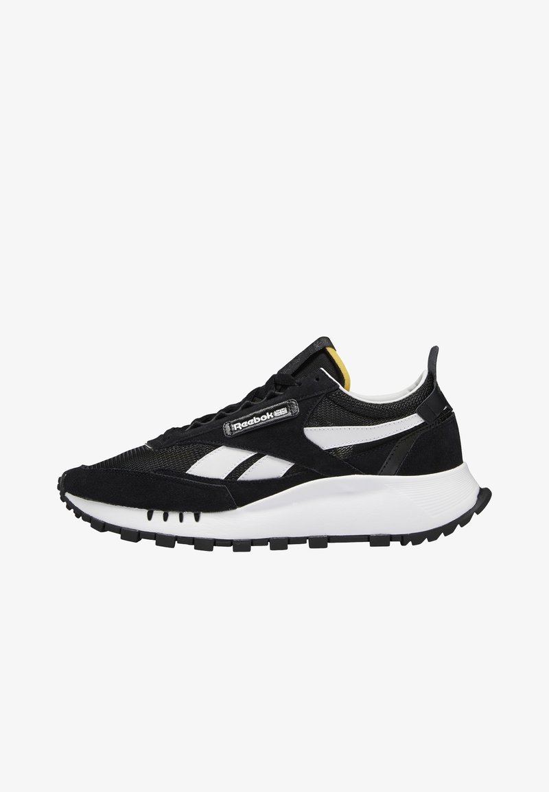 Baskets Reebok noir et blanc avec une semelle blanche épaisse, dessus en mesh et daim, bandes blanches avec logo et petit détail jaune sur la languette.