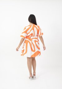 Vestido de manga corta con base blanca y un audaz patrón abstracto en color naranja, cintura elástica y silueta fluida. Sandalias de tacón alto transparentes.