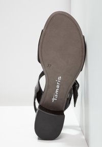 Semelle de sandale noire pour femmes, taille 37, avec le nom de la marque "Tamaris" visible, montrant une semelle lisse et un talon carré.