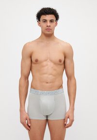 Grå boksershorts med et blått elastisk livbånd som har "ARMOR" i fet skrift. Glatt tekstur, tettsittende design og dekning til midt på låret.