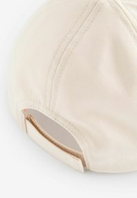 Gorra de béisbol beige con una textura de tela suave, que presenta un visor curvado y una correa ajustable en la parte posterior para un ajuste del tamaño.