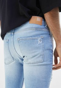 Ljusblå denimjeans med en blekt utseende, med en sliten ficka, kontrastsömmar och ett tan-färgat lädermärke med varumärket på baksidan.