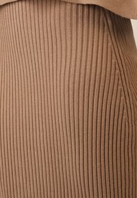 Brauner gerippter Strickstoff mit vertikalen Streifen. Weiche Textur, figurbetontes Design und sichtbare Nähte entlang der Kanten.