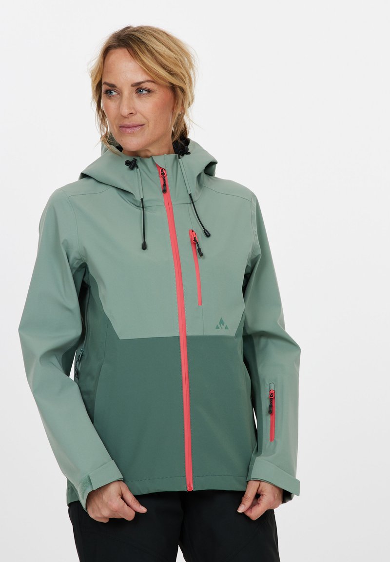 Veste imperméable en vert clair avec panneaux vert foncé ; comprend une capuche, des poches zippées et des accents de fermeture éclair rouges contrastants.