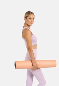 Lavendel sportbeha en hoge taillelegging, houdt een opgerolde perzikkleurige yogamat vast. Gladde textuur, aansluitend ontwerp en neutrale achtergrond.