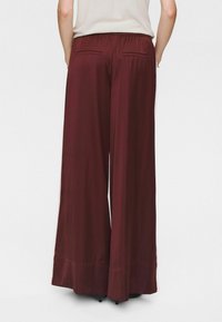 Pantaloni larghi color bordeaux con vita elasticizzata, texture liscia e due tasche posteriori. L'orlo è leggermente svasato nella parte inferiore.