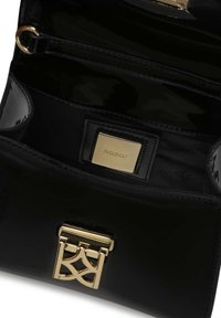 Crna lakirana torba s teksturiranim unutrašnjim dijelom. Ima zlatni logo i zlatne dijelove. Više kompartmana za organizaciju.