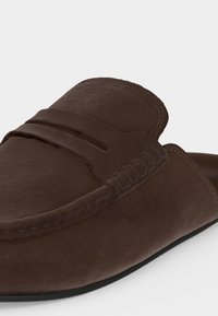 Καφέ μοκασίνι από σουέτ με λουράκι τύπου penny και λεπτομερείς ραφές κατά μήκος των άκρων, εμφανίζεται σε απλό φόντο.