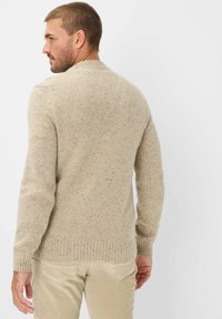Beige Strickpullover mit einem strukturierten Muster und gerippten Bündchen. Kombiniert mit hellen Cordhosen, die einen eng anliegenden, lässigen Stil zeigen.