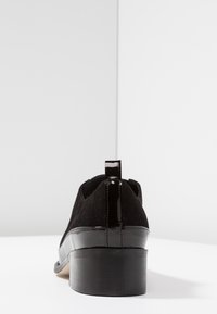 Czarne zamszowe buty z błyszczącym obcasem z lakierowanej skóry. Posiadają małą pętelkę i zaokrąglony czubek, zaprojektowane z myślą o komforcie i stabilności.