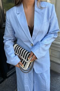 Ljusblå linnékavaj med en knapp, parat med en svart och vit vävd clutch med kedjerem. Subtila texturdetaljer synliga.