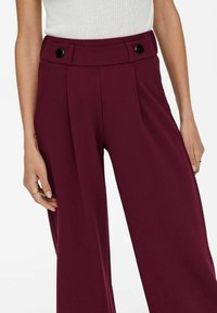 Bordeaux brede pijpenbroek van een gladde stof, met twee voorplooien en een hoge taille met dubbele zwarte knoopaccenten.