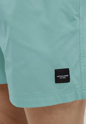 Pantaloni da bagno turchesi realizzati in tessuto leggero, con etichetta nera con la scritta "JACK & JONES EST. 1990" vicino all'orlo e cuciture pulite.