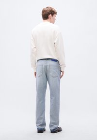 Φούτερ ανοιχτού μπεζ χρώματος με στρογγυλή λαιμόκοψη και ανοιχτό γαλάζιο φαρδύ τζιν παντελόνι, με σκουρό μπλε ζώνη μέσης που φέρει το ανάγλυφο λογότυπο "HUGO".