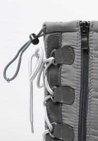 Bota aislante gris con parte superior de tela acolchada, cierre de cremallera y cordones ajustables. Presenta detalles en cuero y una parte superior redondeada.