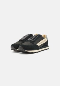 Adidași din suede negru și plasă, cu șireturi gri și accente crem. Dispune de un logo pe lateral și o talpă texturată din cauciuc pentru aderență.