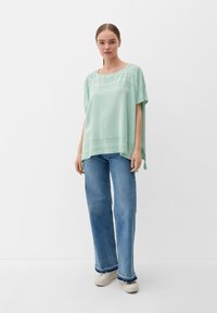 Licht muntgroene, loszittende top met korte mouwen, voorzien van uitsnijdingen langs de halslijn en de zoom. Gepaarde met hoge taille, wijde jeans.