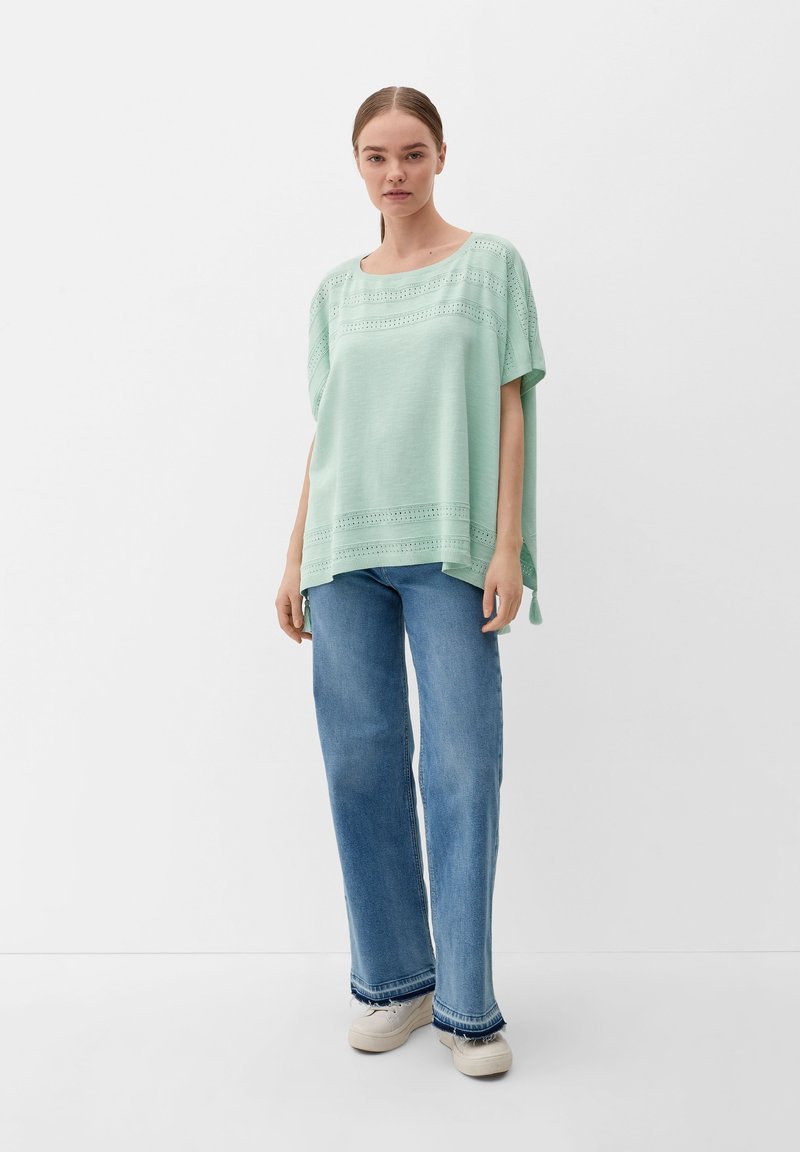 Licht muntgroene, loszittende top met korte mouwen, voorzien van uitsnijdingen langs de halslijn en de zoom. Gepaarde met hoge taille, wijde jeans.