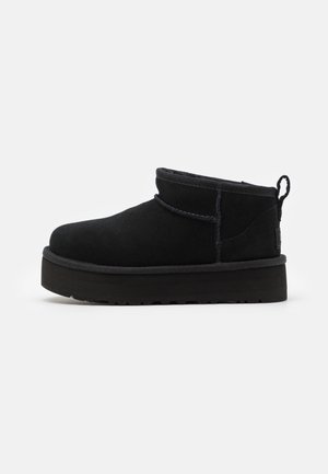 Botas ankle de camurça preta com bico redondo, gola alta e alça para puxar, apresentando uma sola grossa de borracha preta texturizada.