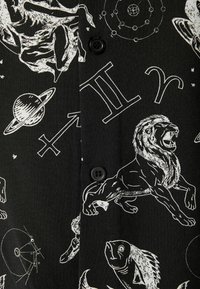 Tela negra con ilustraciones blancas de símbolos astrológicos, leones, planetas y figuras. Detalles que incluyen un botón frontal y patrones intrincados.