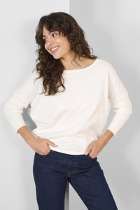 Cremefarvet strikket sweater med en bred halsudskæring og ribbede mansjetter, parret med mørkeblå denimbukser. Glat tekstur, afslappet pasform.