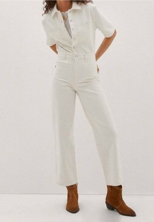 Biały kombinezon z denimu z krótkimi rękawami, zapinany na guziki z przodu, z prostymi nogawkami, w zestawieniu z brązowymi botkami do kostki ozdobionymi ćwiekami.