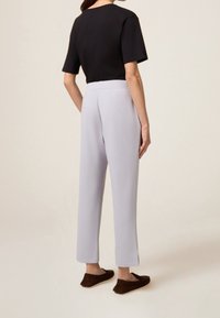 Černý top s krátkým rukávem, světle šedé přizpůsobené kalhoty s bočními rozparky, měkká textura, uvolněný střih, doplněné tmavě hnědými nazouvacími botami.