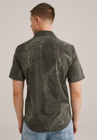Camisa de manga corta de color verde oscuro con un patrón de hojas en verde claro y negro, con un cuello clásico y dobladillo redondeado. Material de algodón.