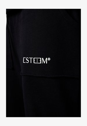 Schwarzer Stoff, zusammengenäht und gefaltet, zeigt das weiße ESTEEM-Logo mit einem eingetragenen Markensymbol, das nahe der Naht gestickt ist.