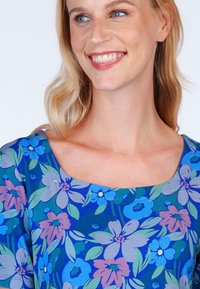 Bluse mit floralem Druck und quadratischem Ausschnitt. Ausstattung mit blau, grün und lila Blumen auf einem dunkelblauen Hintergrund. Weicher, leichter Stoff.