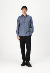 Cămășă albastră cu nasturi, cu mâneci lungi, având un model subtil și o croială ajustată, asortată cu pantaloni negri cu croială dreaptă și cizme negre.