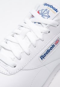Baskets en cuir blanc avec lacets plats, col rembourré et logo Reebok. Dotées d'un accent de logo bleu et rouge ainsi que d'une surface texturée.