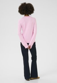 Lichtroze, lange mouwen trui met een ronde hals. Gecombineerd met donkerblauwe flared jeans en bruine laarzen. Soepele textuur en aansluitend ontwerp.