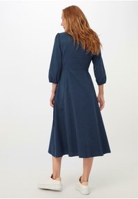Dunkelblaues, knielanges Kleid mit drei Viertel-Puffärmeln und tailliertem Oberteil. Weicher Stoff und subtile Nahtdetails auf der Rückseite.