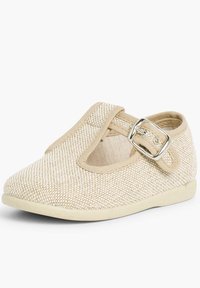 Zapato Mary Jane de lona beige con punta redondeada, correa ajustable con hebilla y diseño tejido texturizado en la parte superior. Suela plana de goma.
