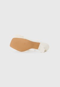 Scarpa bianca con tacco quadrato, suola texturizzata e dettagli in pizzo. Materiale superiore liscio con design minimalista.
