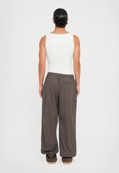 Hvid tanktop parret med løse, mørkegrå bukser med elastisk talje og baglomme. Blød tekstur; minimalistisk design.