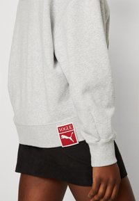 Felpa grigia in misto cotone, con polsini e orlo a costine, dotata di un patch rosso con il logo 'VOGUE' e la silhouette Puma.