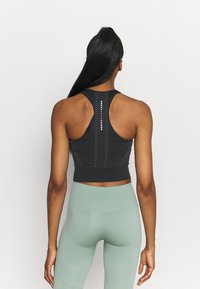 Top corto atletico nero con design a schiena scoperta, dotato di pannelli in rete e strisce riflettenti. Abbinato a leggins verde chiaro a vita alta.